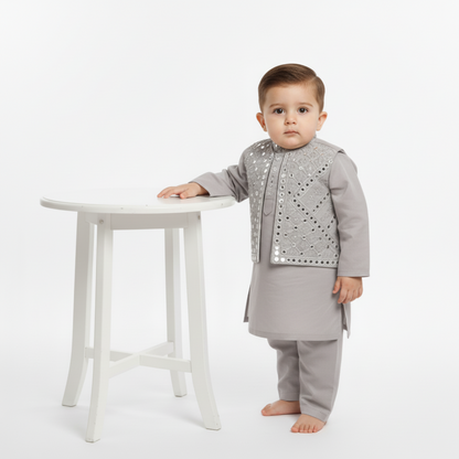 Child wearing a gray outfit with decorative elements standing next to a small white table on a white background
